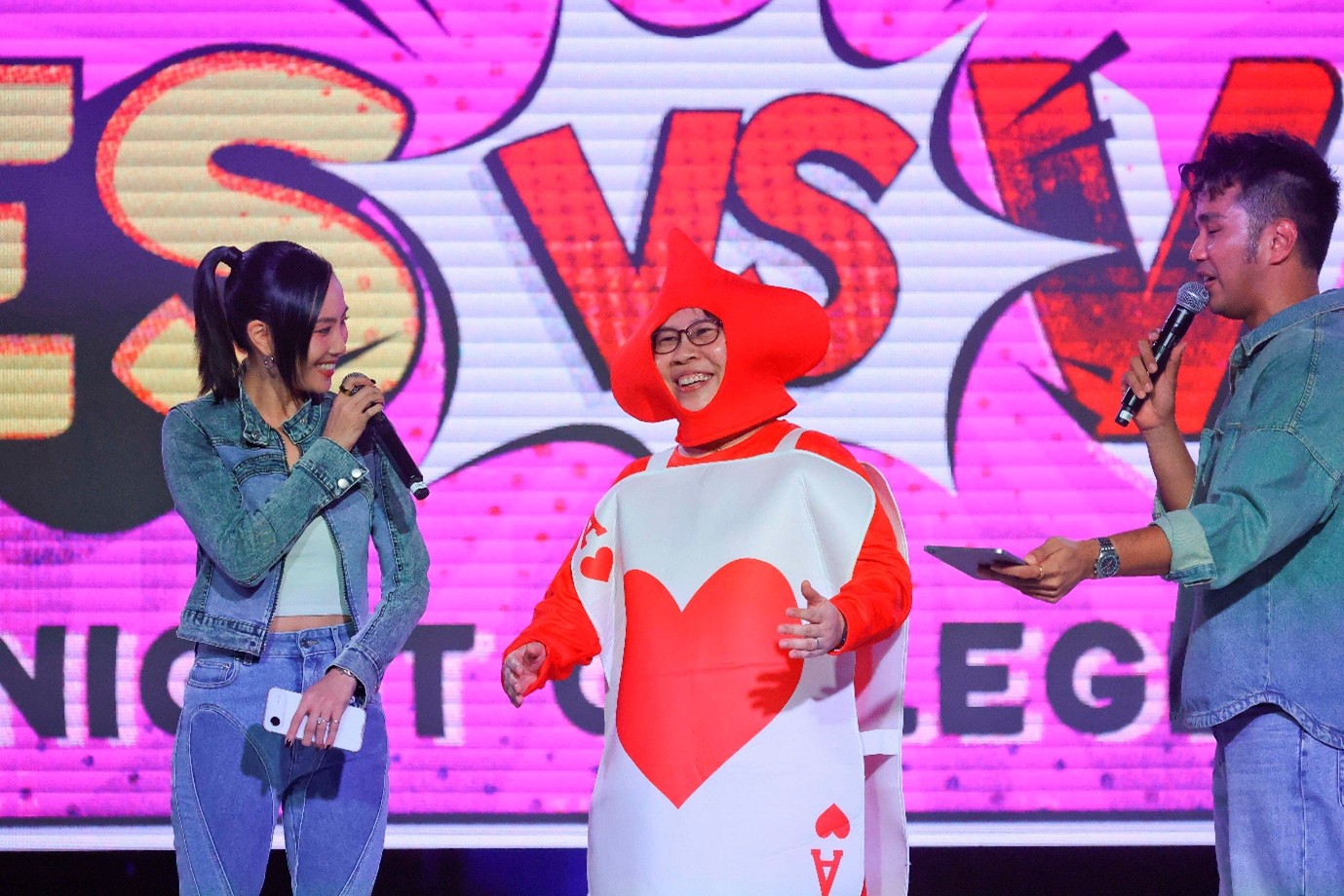 A person in a costume speaks to two people dressed in denim and holding microphones.