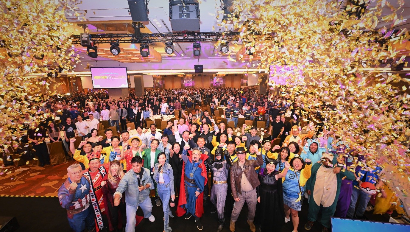 A large group of people packed into a ballroom, celebrating under a shower of golden confetti.
