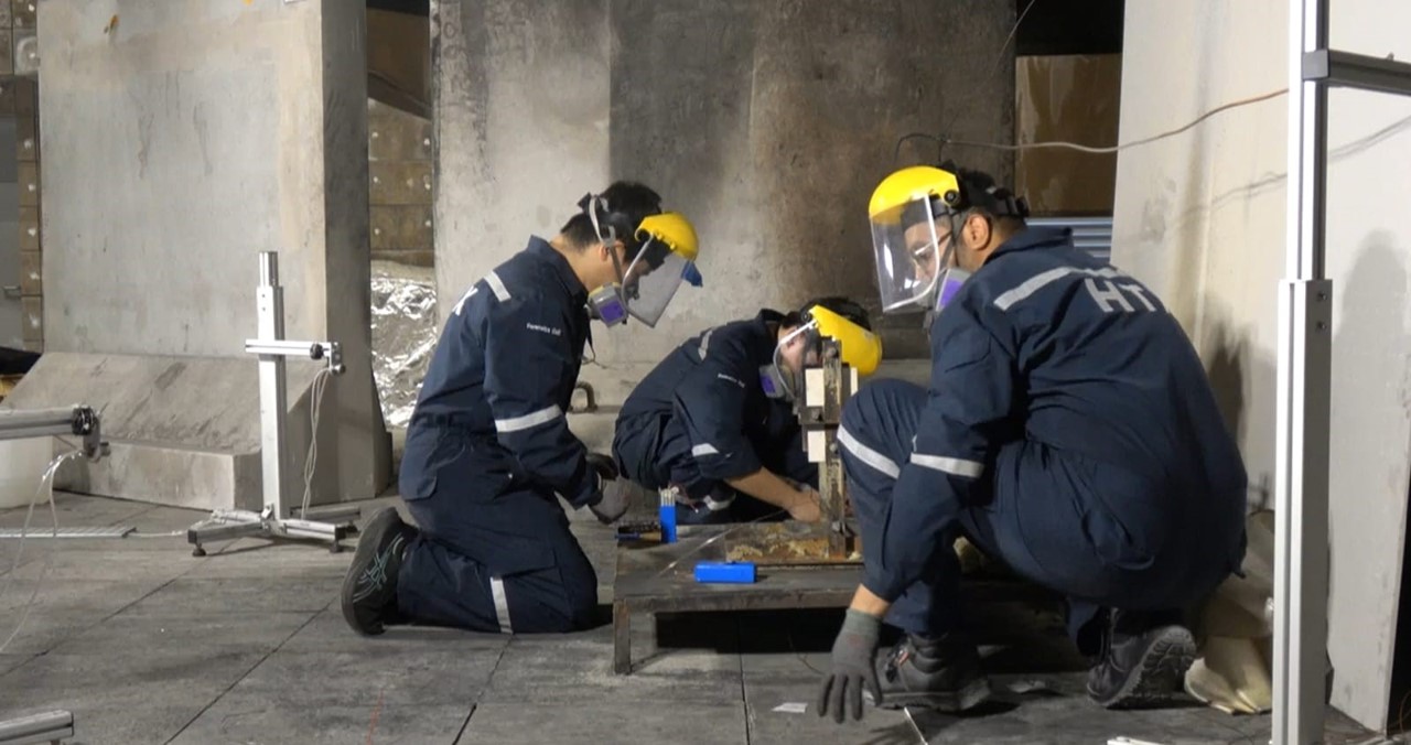 A group of people wearing overalls and facial protective gear and working with raw materials in an industrial setting.