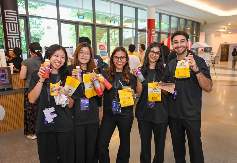 Five young adults hold up bottles of juice and yellow bags from a food vendor at the event.