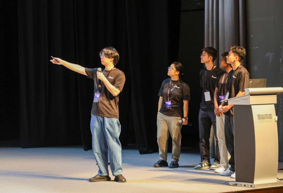 A man with a microphone and a few other people on stage, with the man pointing off-stage.