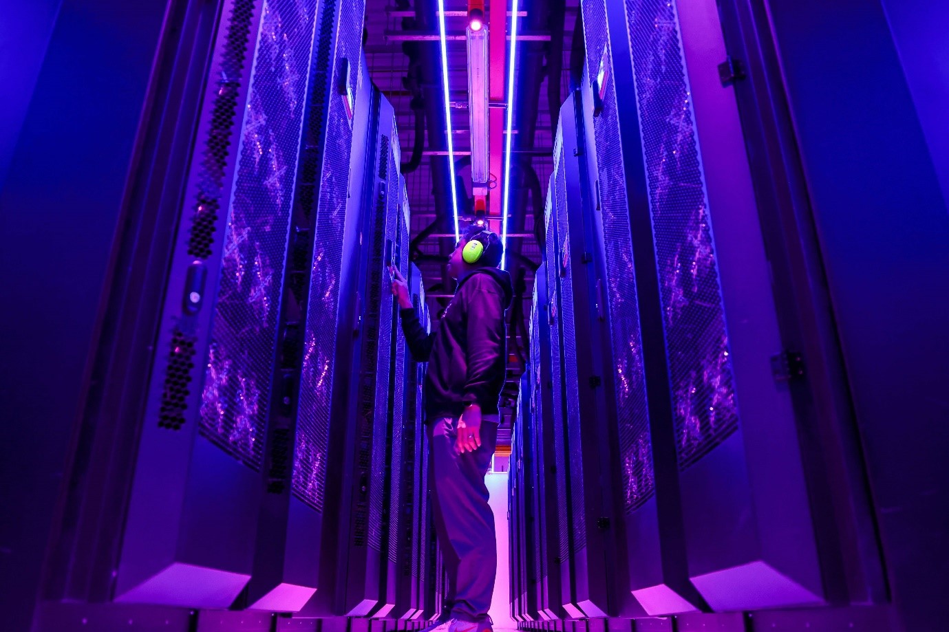 A person standing in a room with rows of servers.