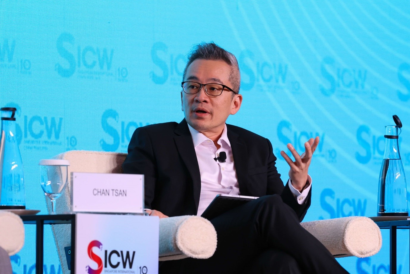 A man in a suit speaks during a panel discussion at Singapore International Cyber Week, gesturing while holding a tablet.