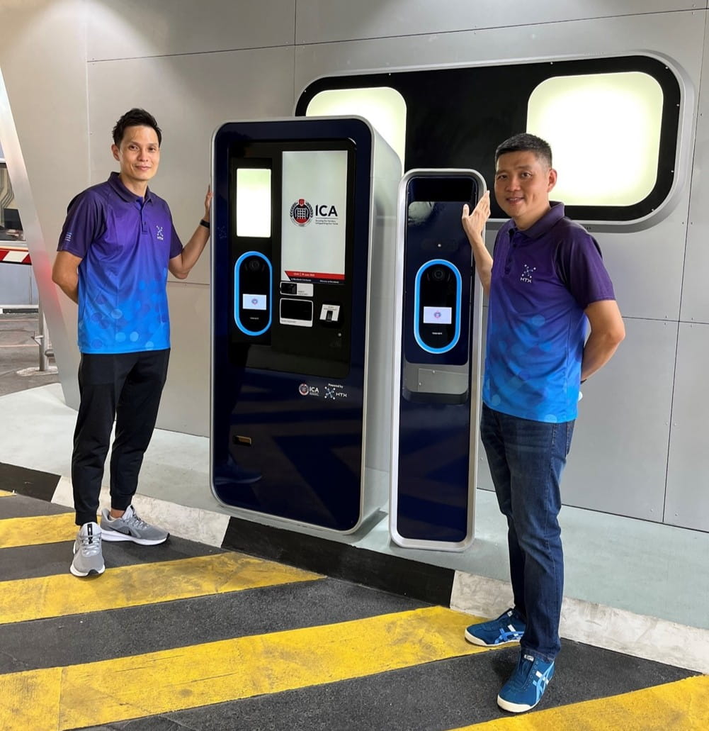 Two men standing beside an electronic kiosk.