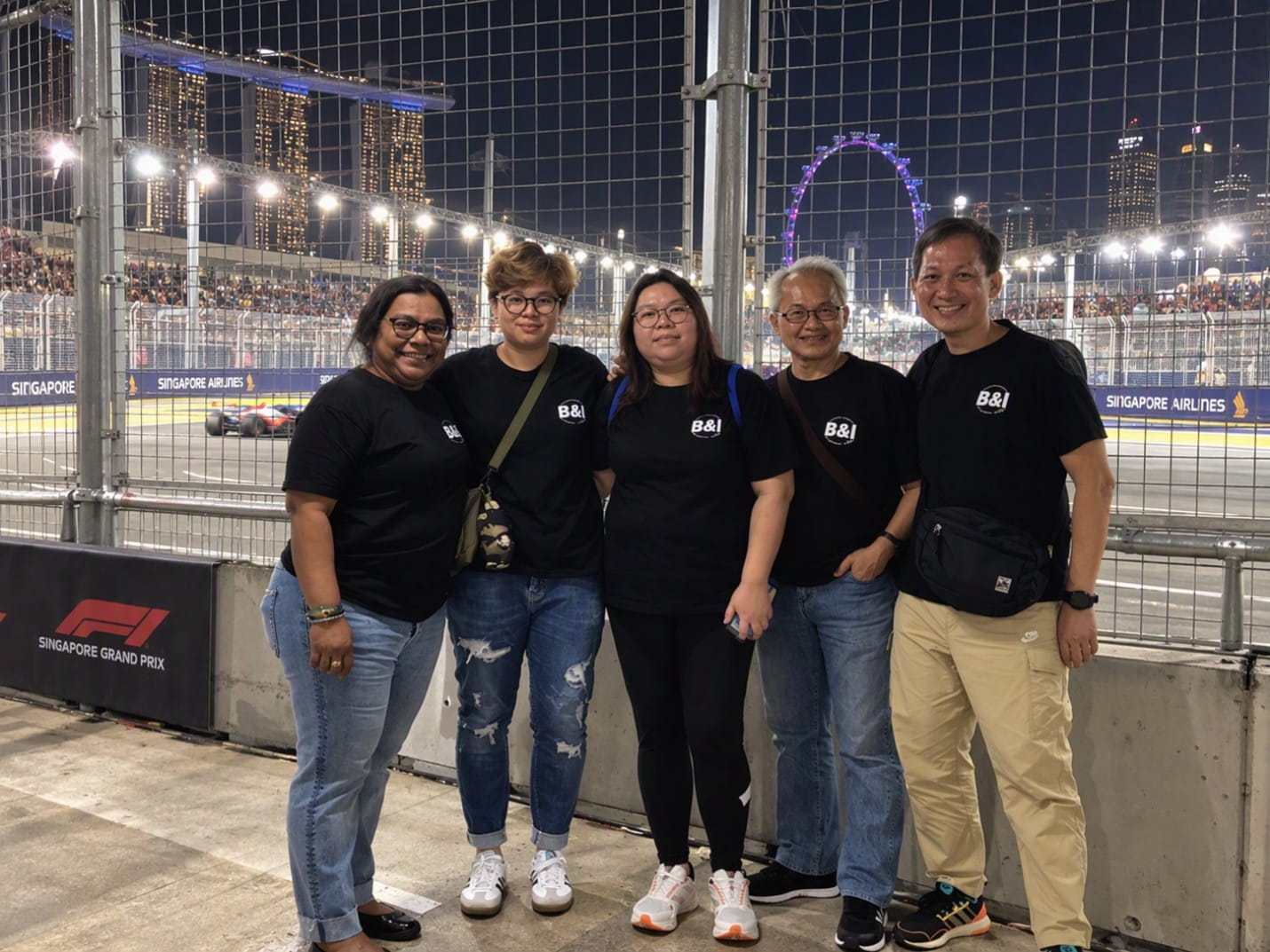 Group of people posing beside a nighttime Singapore Grand Prix street circuit.