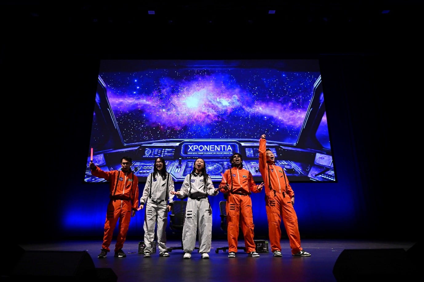 Five people on stage wearing astronaut suits in orange and white.