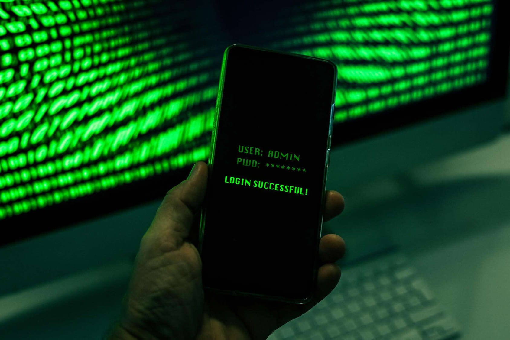 A hand holding a smartphone with a green text login screen displaying "User: Admin", obscured password, and "Login successful!"