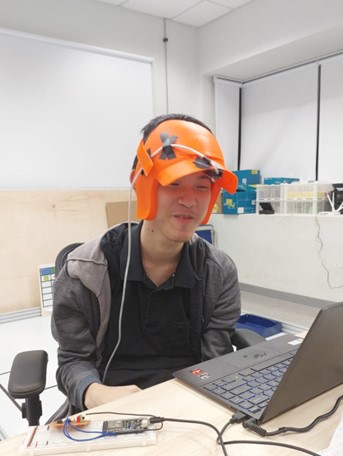 A young man wearing an orange helmet, sitting at a desk with a computer.