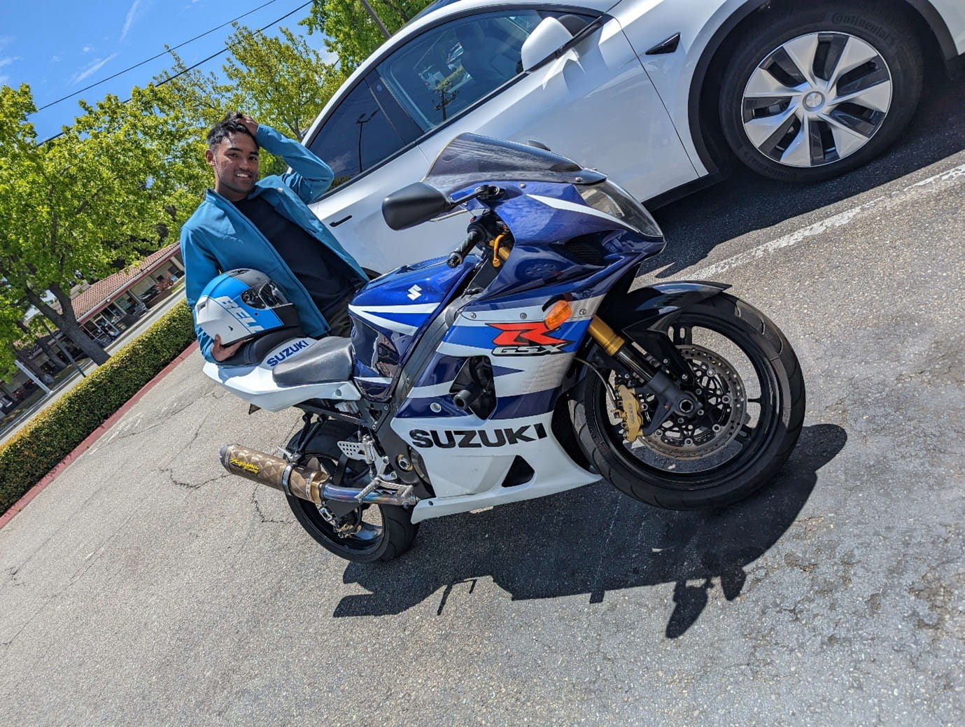 A man posing in a parking lot next to a blue and white motorcycle.