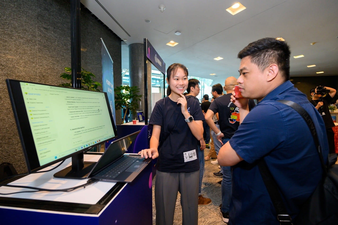 A woman demonstrating a software interface on a monitor screen to a man at an exhibition booth.